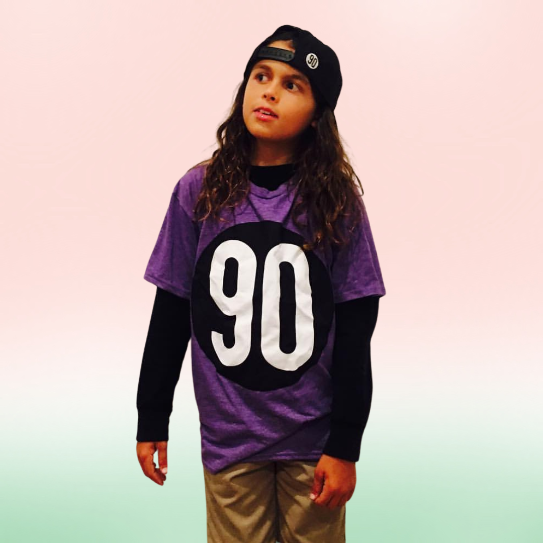 Child model wearing the purple 90 The Original Kids Tee with matching black hat.