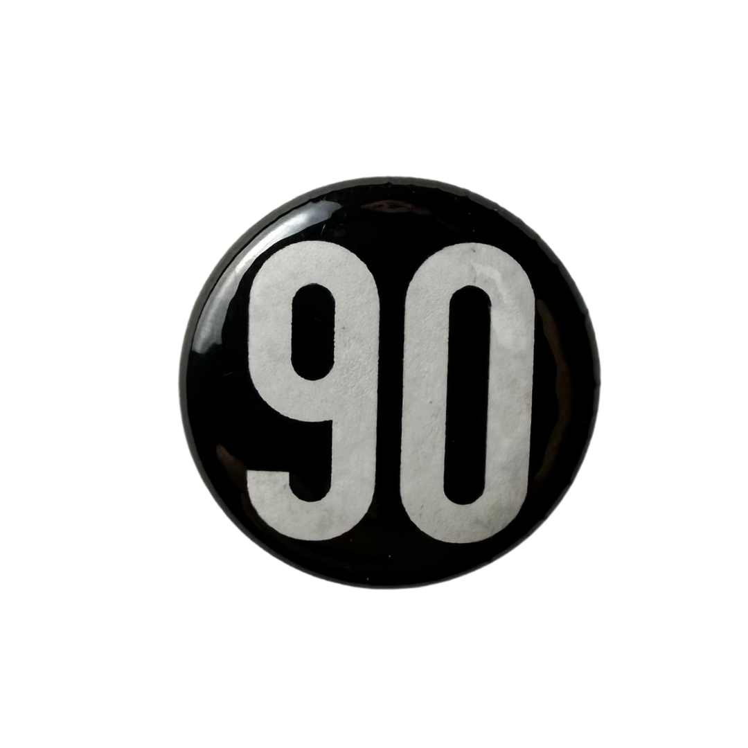 Sleek black 90 The Original enamel pin with contrasting logo.